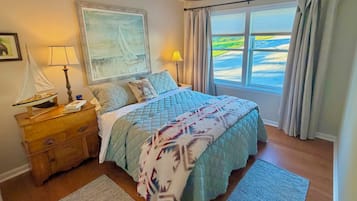 Een slaapkamer met een bed, nachtkastje, lamp, schilderij en uitzicht op de omgeving.