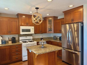 A kitchen with wooden cabinets, a stainless steel refrigerator, a microwave, a stove, and granite countertops.