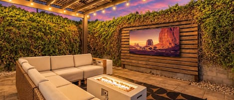 Een terras met zitgedeelte, een vuurkorf en een aan de muur bevestigde televisie.