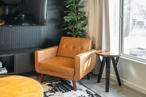 A room with a leather armchair, a small round table, a potted plant, and a large window. - NEW| The Tipsy Cactus Old Town Oasis|Pool+Bar+Putt (Scottsdale)
