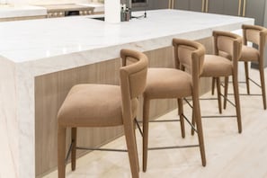 A modern kitchen with a marble countertop and four bar stools with cushioned seats. - Mariposa Social Luxe Old Town Villa (Scottsdale)