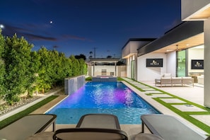 An outdoor swimming pool with a waterfall feature, surrounded by a well-maintained garden and modern outdoor furniture. - Mariposa Social Luxe Old Town Villa (Scottsdale)