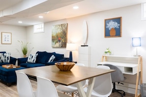 A modern living room with a dining table, blue sofas, white chairs, and artwork on the walls. - Sciota Suite | Private Entrance & Workspace (Peoria Heights)