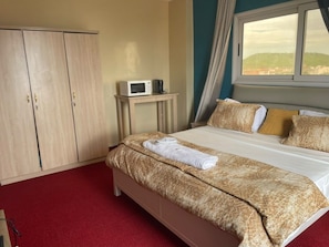 Une chambre d’hôtel comprenant un lit, une armoire, une table de chevet avec un micro-ondes et une fenêtre donnant sur un paysage agréable.
