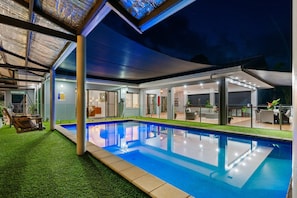 Un área de piscina moderna al aire libre con una silla hamaca, un espacio de estar cubierto y vistas a la piscina.