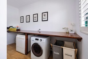 A laundry area with a washing machine, a dryer, and a wooden shelf with folded clothes and a vase of flowers.