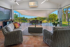 A spacious outdoor seating area with wicker furniture, a flat-screen TV, and a view of a golf course.
