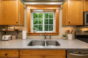 A kitchen with wooden cabinets, a double sink, a window with a view of greenery, a toaster, and a microwave. - Cranmore & Story Land Hot Tub + Sauna Sleeps 10 (Conway)