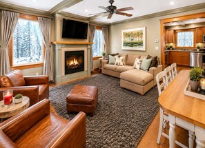 A living room with a fireplace, a television, a sofa, and a dining area with a wooden table and chairs. - Cranmore & Story Land Hot Tub + Sauna Sleeps 10 (Conway)