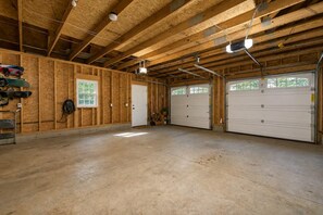 A spacious garage with wooden walls, two garage doors, and a concrete floor. - Cranmore & Story Land Hot Tub + Sauna Sleeps 10 (Conway)