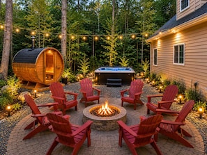 Una bañera de hidromasaje de madera rodeada de sillas Adirondack rojas, un brasero y luces colgantes en un patio.