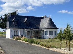 Une maison à deux étages avec une grande véranda à l’avant, un garage et une pelouse bien entretenue.