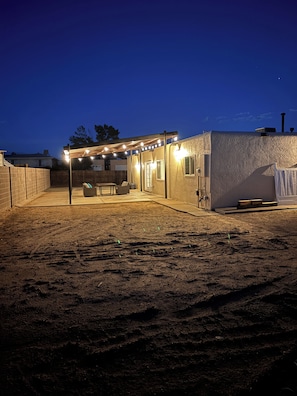 A covered patio area with a seating arrangement and a pergola with string lights. - Come relax, recharge at Desert Oasis. (Rio Rancho)