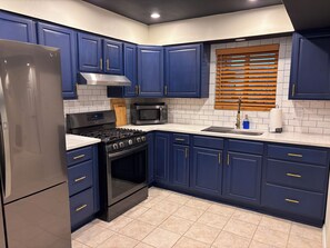 A kitchen with dark blue cabinets, a stainless steel refrigerator, a microwave, a stove, and a window with blinds. - Come relax, recharge at Desert Oasis. (Rio Rancho)