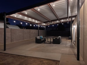 An outdoor patio with a covered seating area, a table, and a brick wall. - Come relax, recharge at Desert Oasis. (Rio Rancho)