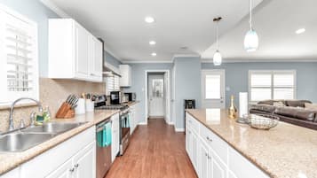 A modern kitchen with white cabinets, a granite countertop, and a wooden floor.