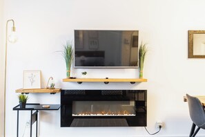 A modern living room with a flat-screen TV mounted above a fireplace, flanked by two potted plants. - Loft Doré | Montmorency Falls (Boischatel)