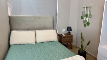 A bedroom with a bed, a nightstand, a lamp, a wall-mounted plant, and a potted plant.