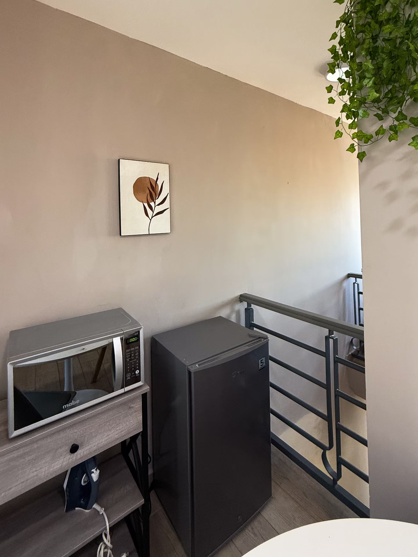 Una kitchenette con microondas y un refrigerador pequeño, una obra de arte colgada en la pared y una baranda de metal.