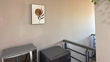 Una kitchenette con microondas y un refrigerador pequeño, una obra de arte colgada en la pared y una baranda de metal.