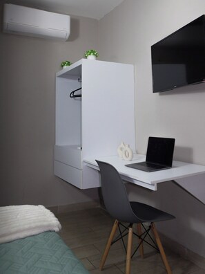 A bedroom with a bed, a desk with a laptop, a wardrobe, and a TV mounted on the wall. - Casa Nordica (Monterrey)