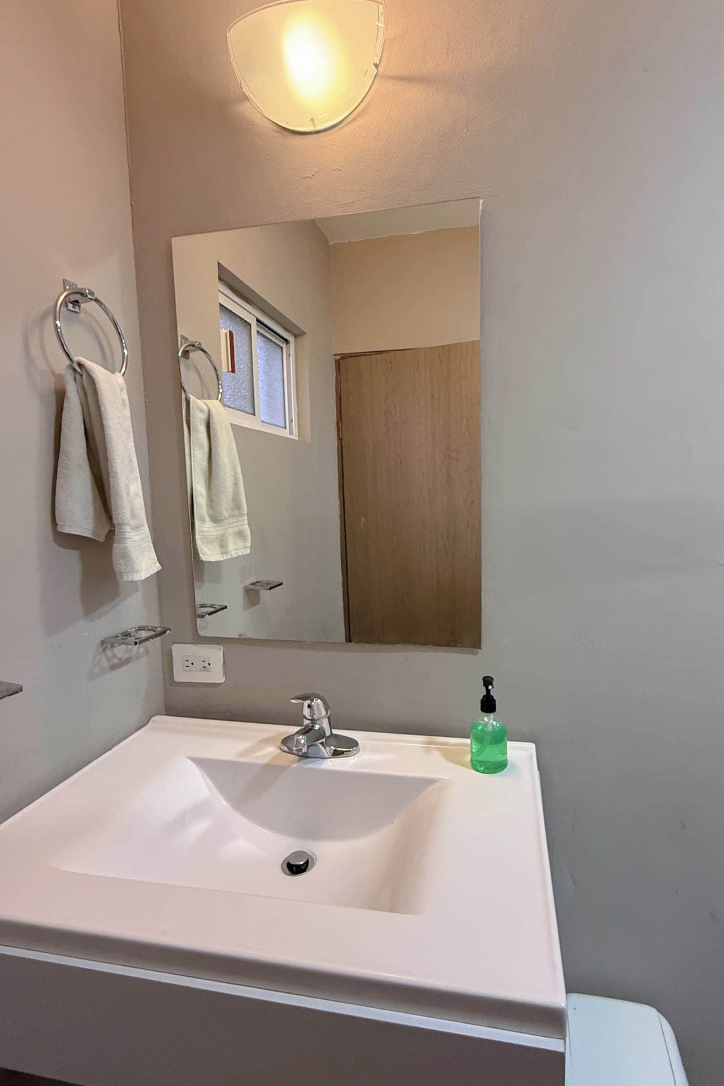 A bathroom with a white sink, a mirror, a towel rack, and a soap dispenser.