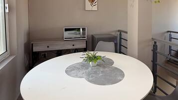 Una mesa redonda de comedor con mantel blanco, dos individuales grises y una planta en maceta en el centro.