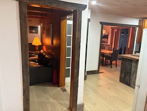 A room with a wooden floor, a dining area with chairs and a table, and a kitchen area with a refrigerator.