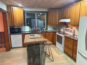 A kitchen with wooden cabinets, a microwave, a dishwasher, a stove, and a wooden island with stools.