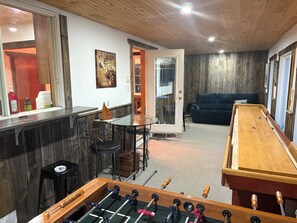A room with a foosball table, a bar area, and a sofa.
