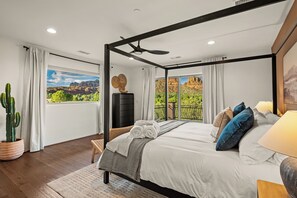 Ein Himmelbett mit Blick auf eine gebirgige Landschaft durch große Fenster.