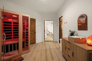 Ein Flur mit Holzboden, ein Saunaraum mit roten Glastüren, eine Holzvertäfelung mit einer Salzlampe und ein Poster an der Wand.
