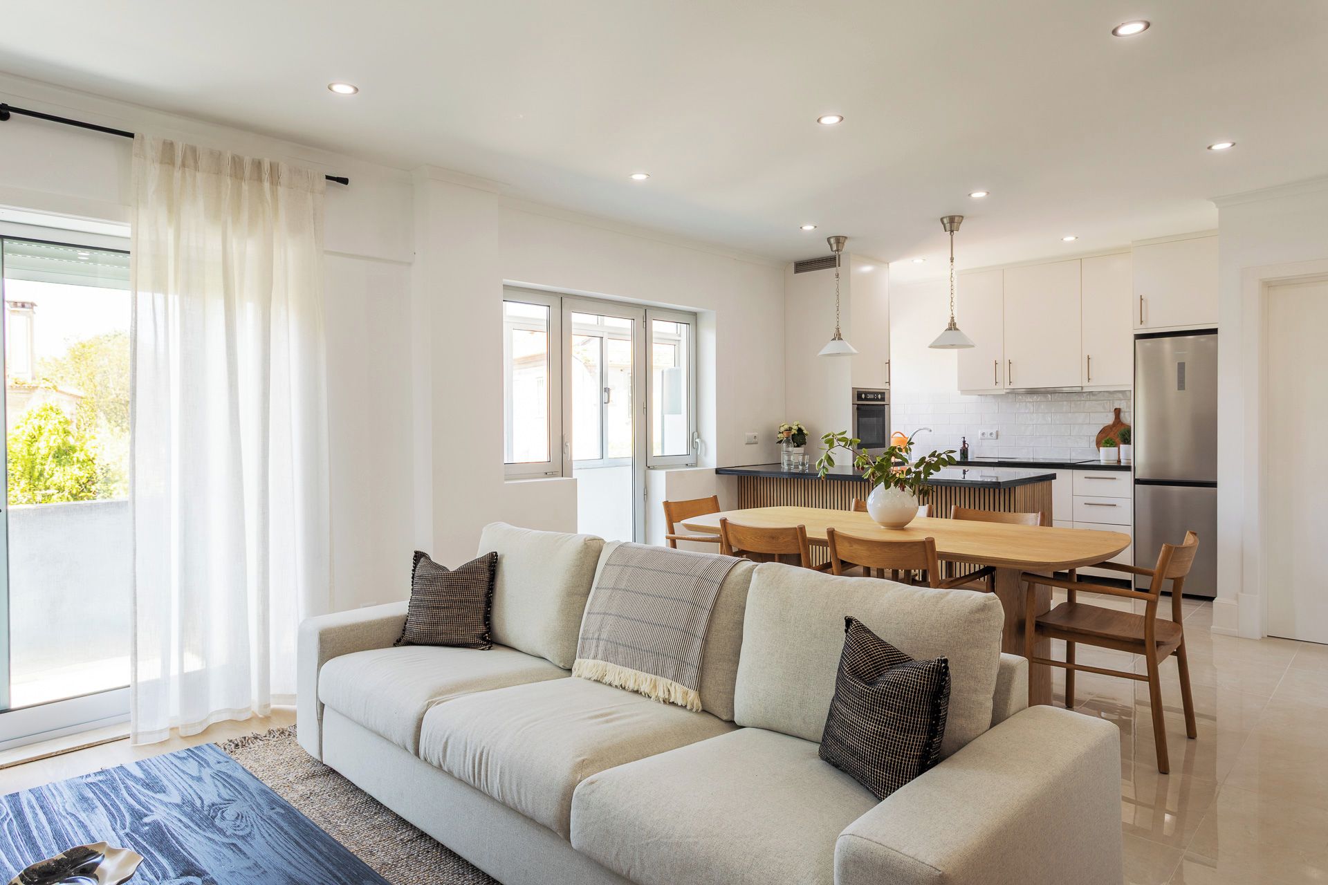 Una sala de estar moderna con sofá, mesa de comedor y zona de cocina con refrigerador.