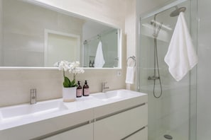 A bathroom with a glass shower enclosure, a large mirror, and a white sink with two bottles of lotion. - Stylish Central Aveiro Stay | 3BR + Office (Aveiro)