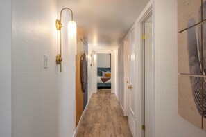 A hallway with wooden flooring, white walls, and a bed with a blue headboard in the background. - Heatwave HQ-Sport Court, Gym, Pool/SPA, Speakeasy (Scottsdale)