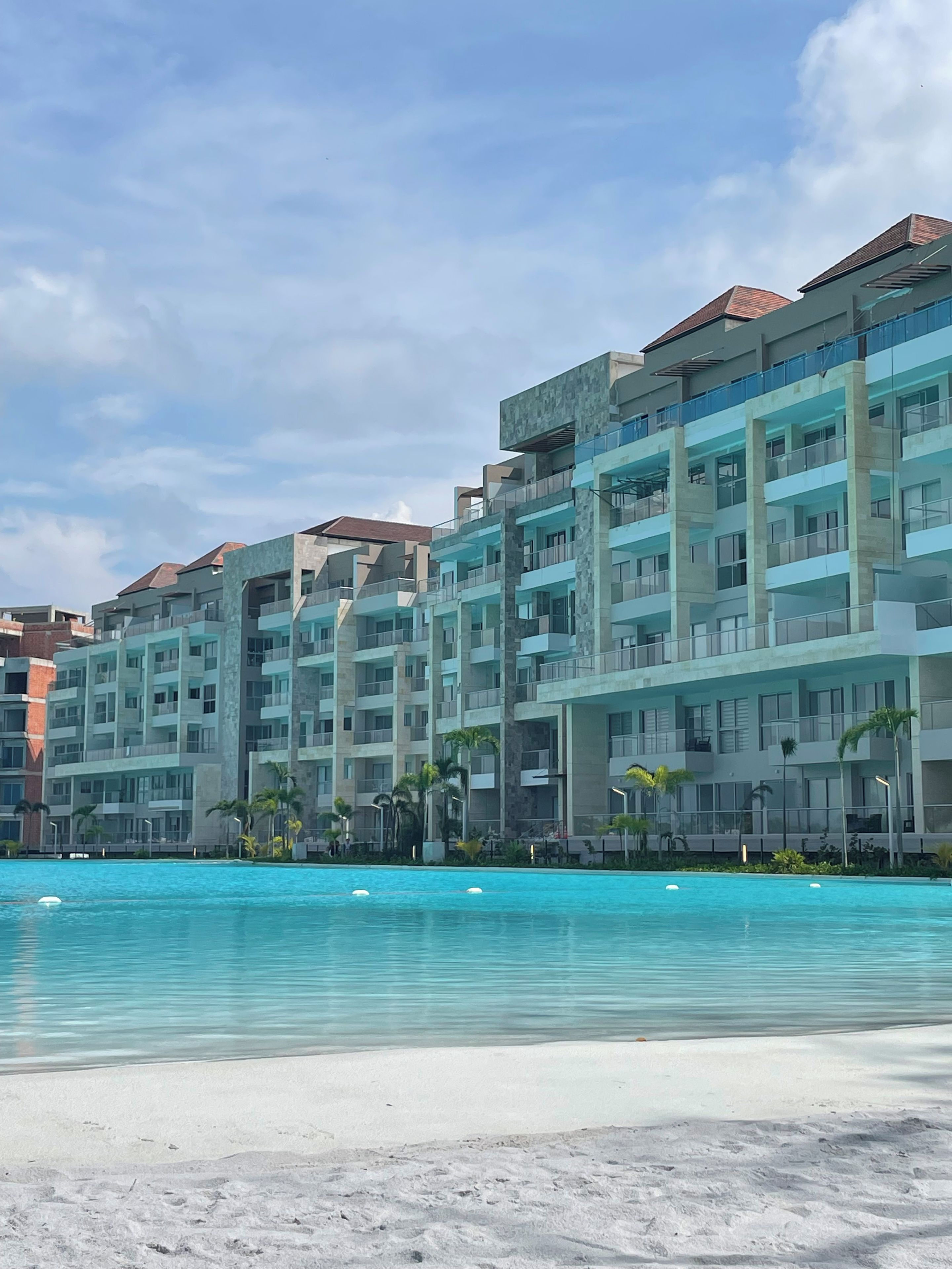 Un hotel frente a la playa con varios balcones, una piscina y una playa de arena.
