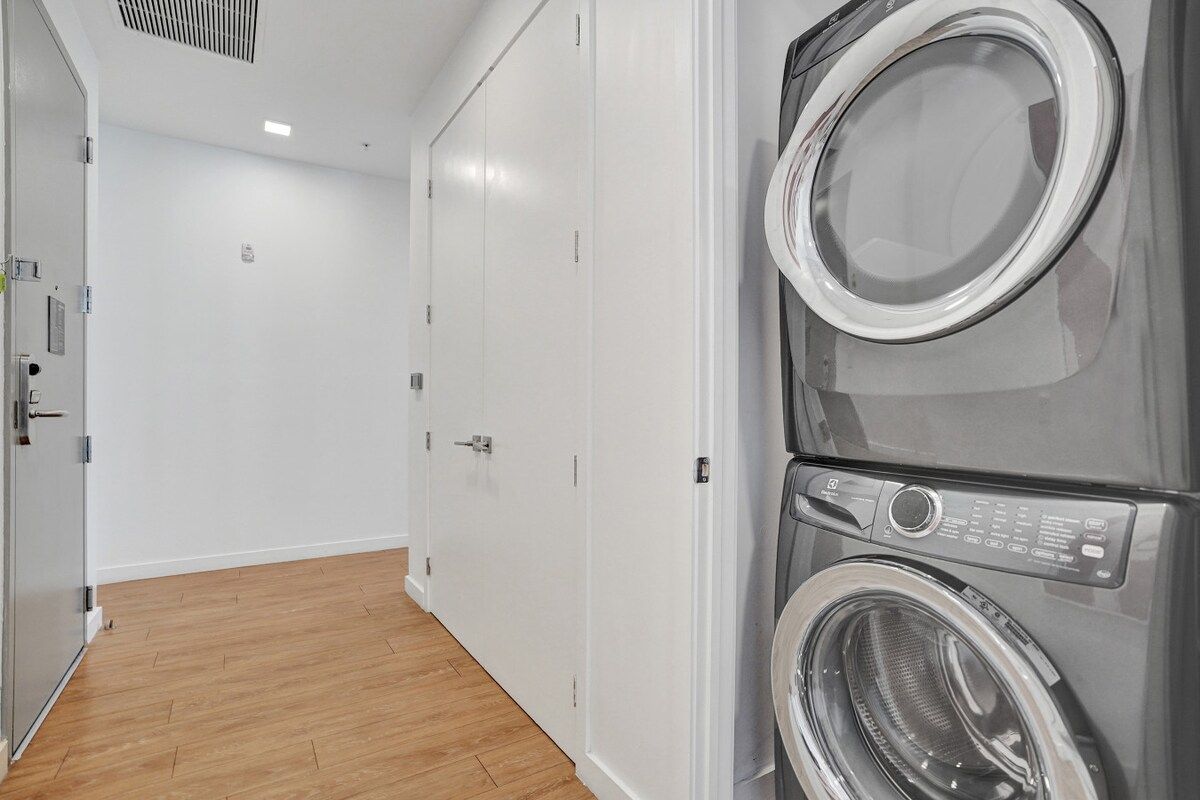 A laundry room with two stacked front-loading washing machines, a door, and a wooden floor.