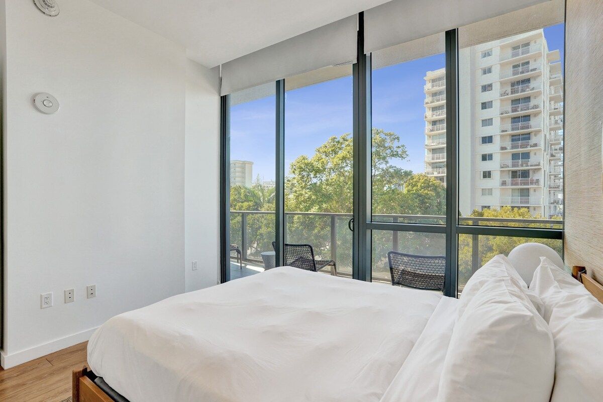 A bedroom with a large bed, a window, and a view of a building.
