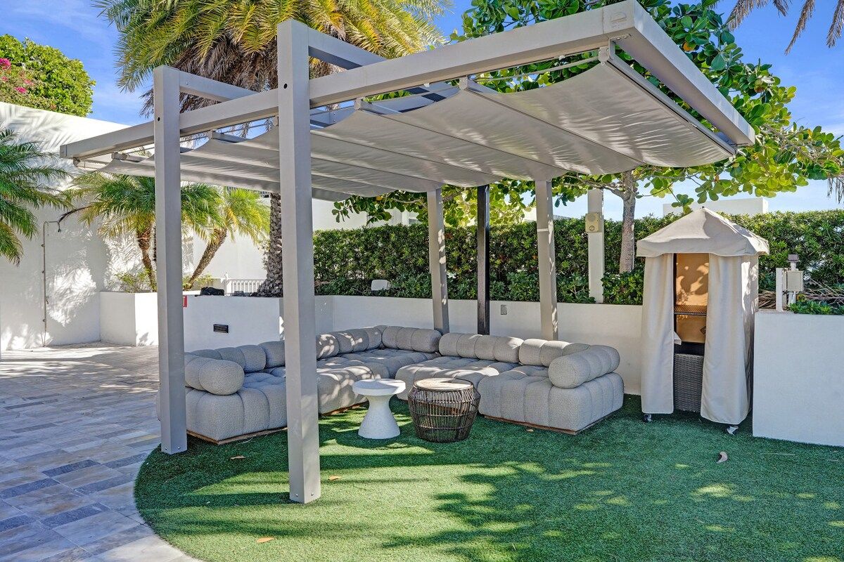 A covered outdoor seating area with a white pergola, a sectional sofa, and a small table.