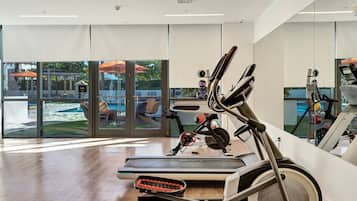 A modern gym with cardio equipment, large windows, and a view of outdoor seating.
