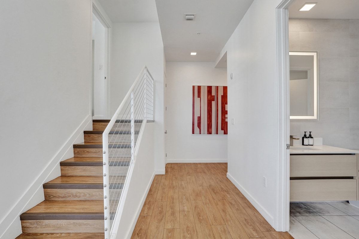 A modern interior with a wooden staircase, a minimalist bathroom, and a red abstract artwork on the wall.