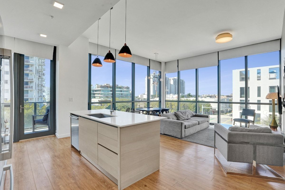 A modern kitchen with a central island, large windows, and a view of the cityscape.