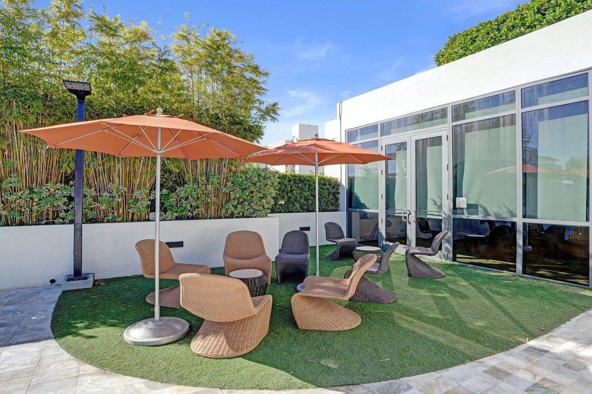 An outdoor seating area with wicker chairs and orange umbrellas, surrounded by a well-maintained lawn and bamboo plants.