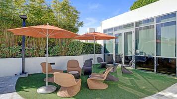 An outdoor seating area with wicker chairs and orange umbrellas, surrounded by a well-maintained lawn and bamboo plants.