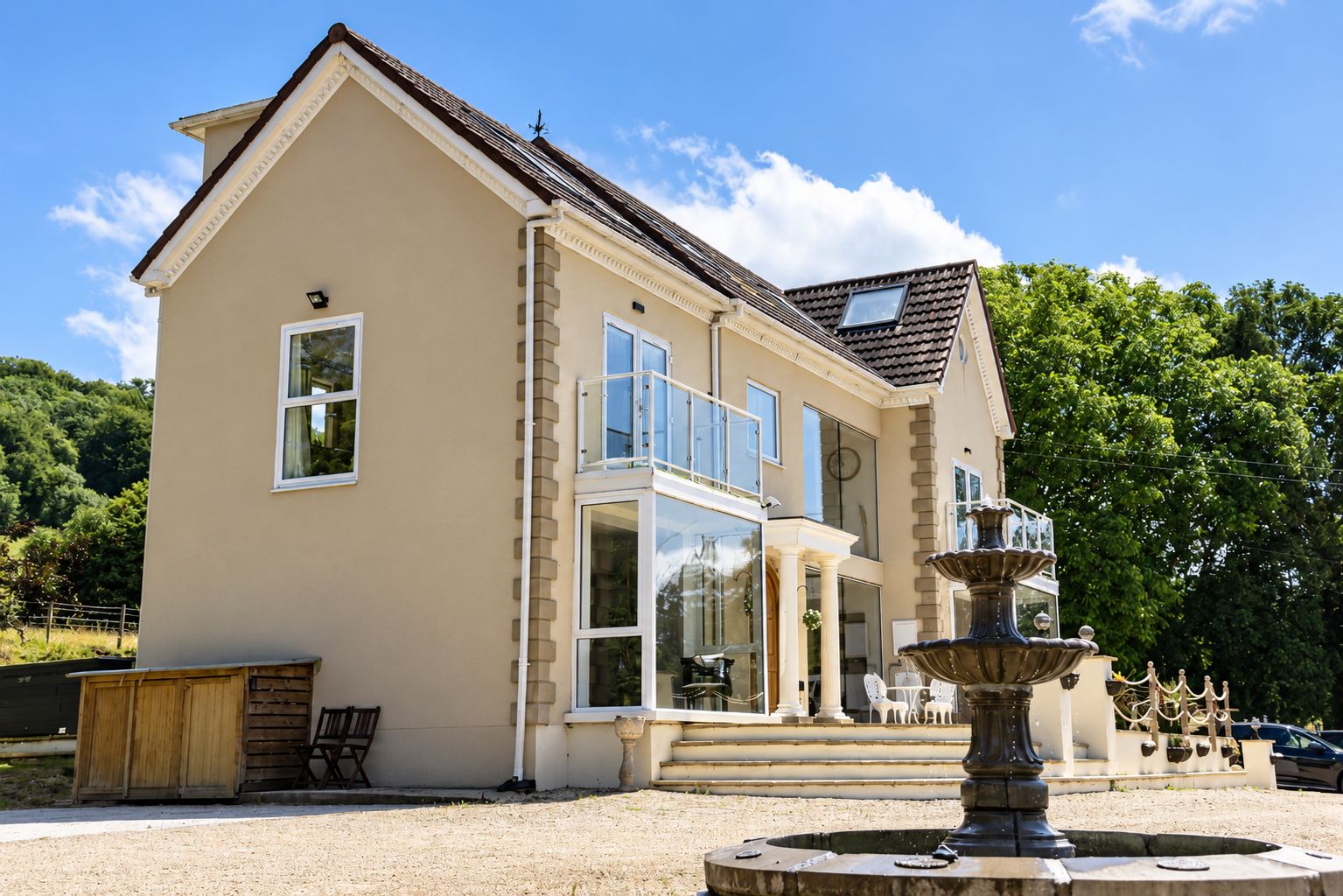 A two-story house with a large balcony, a fountain, and a garden area.