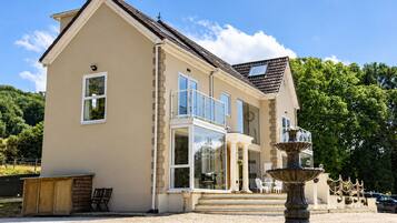 A two-story house with a large balcony, a fountain, and a garden area.