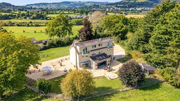 A two-story house with a patio area, surrounded by greenery and a view of a rural landscape.