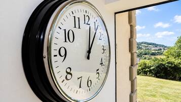 A wall-mounted clock with a clear view of a scenic landscape through an open door.