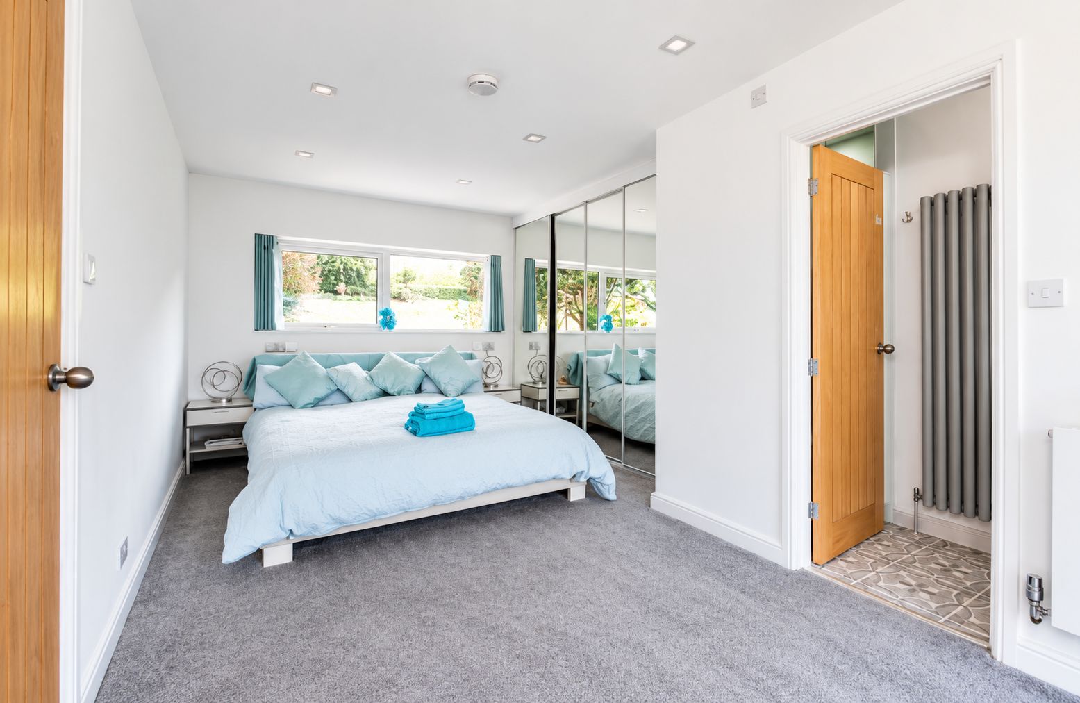 A bedroom with a bed, a bedside table, a mirror, and a window.