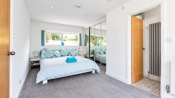 A bedroom with a bed, a bedside table, a mirror, and a window.